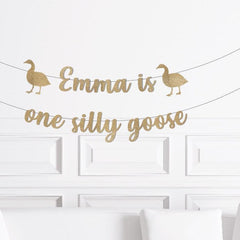 Gold banner with 'Emma is one silly goose' text on a white wall.