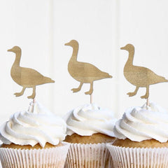 Cupcakes with white frosting and gold duck-shaped toppers on a white background